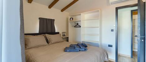 A bedroom with a bed, a wardrobe, a hanging shelf, and an air conditioning unit.