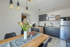 A modern kitchen with a dining area, featuring a wooden table, a vase with flowers, and a stainless steel refrigerator.