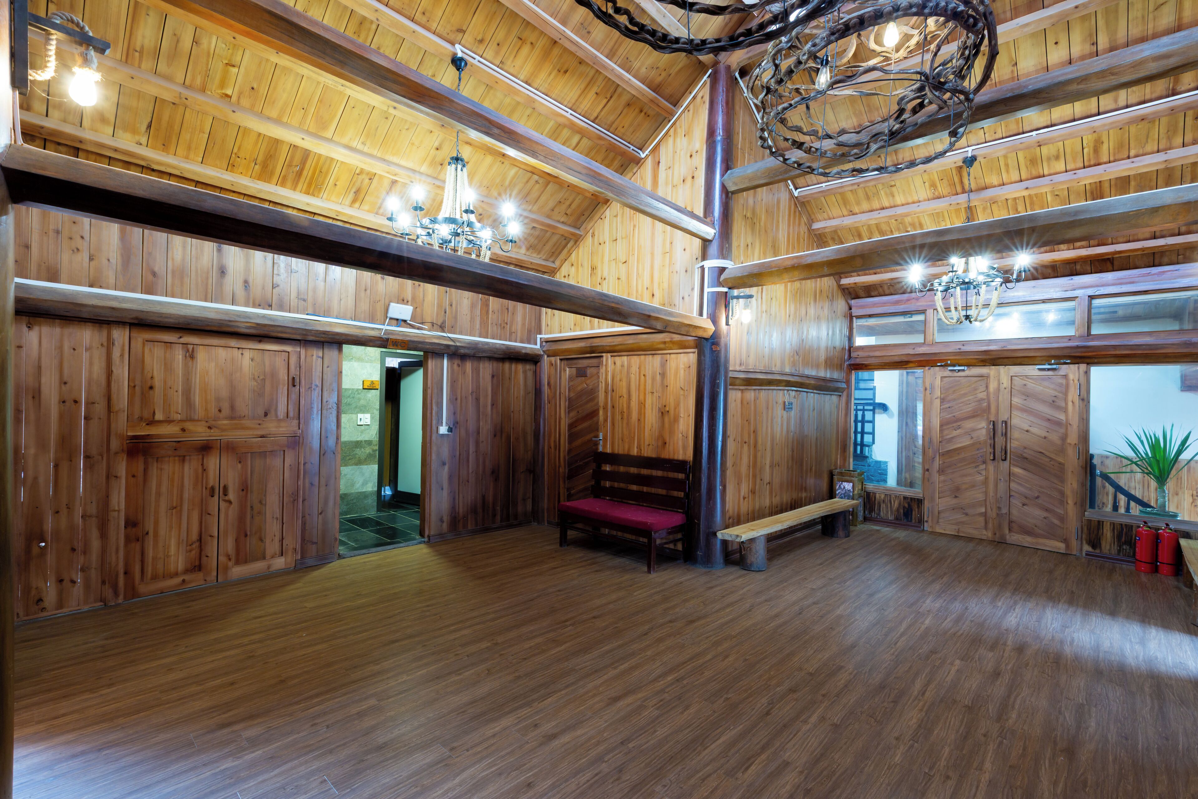 A spacious room with wooden walls and floors, a bench, and a chandelier.