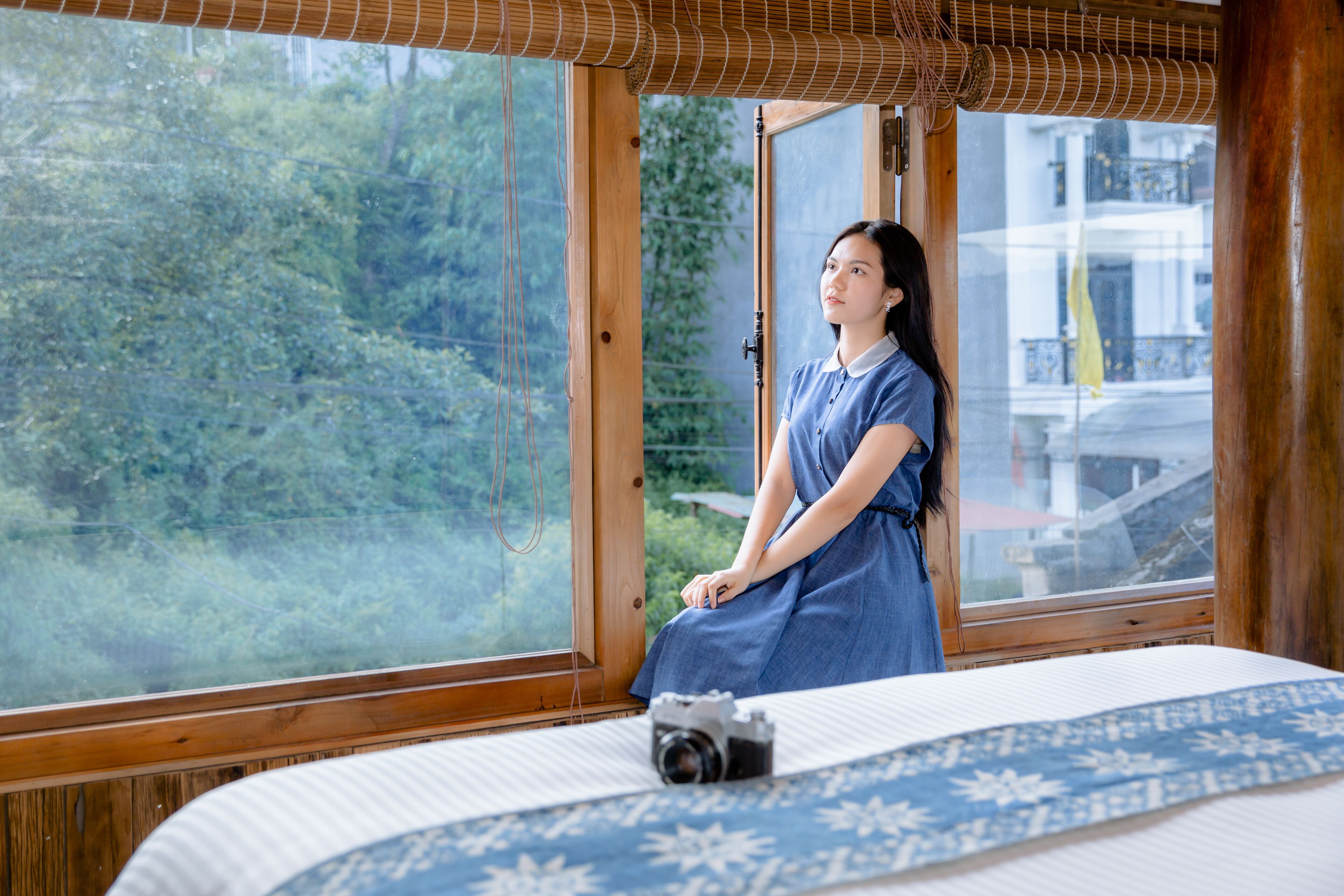 Una habitación con una cama, una cámara sobre la cama y un ventanal con vistas a la vegetación.