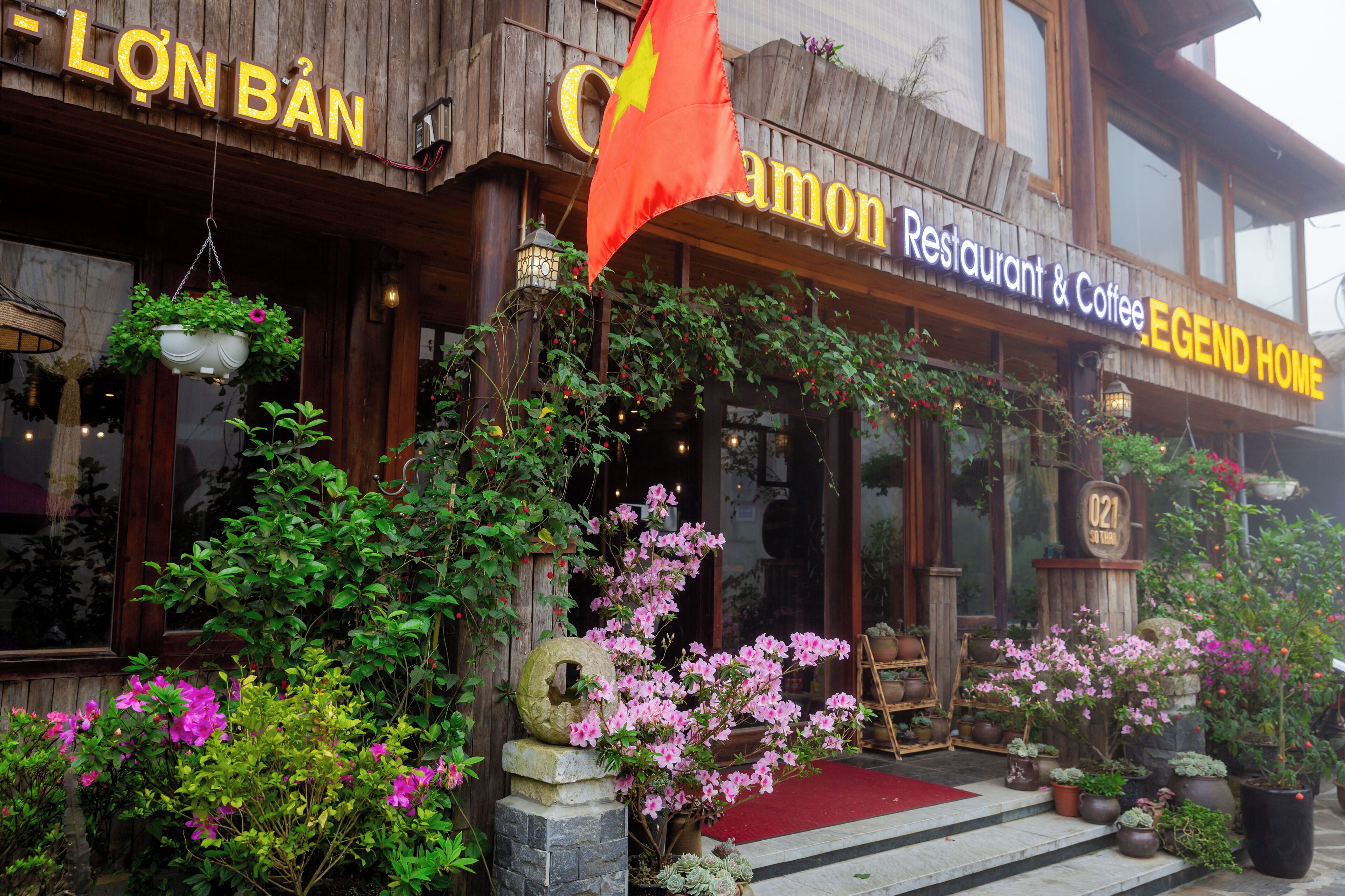 A restaurant with a wooden facade, hanging flower pots, and a red carpet entrance.