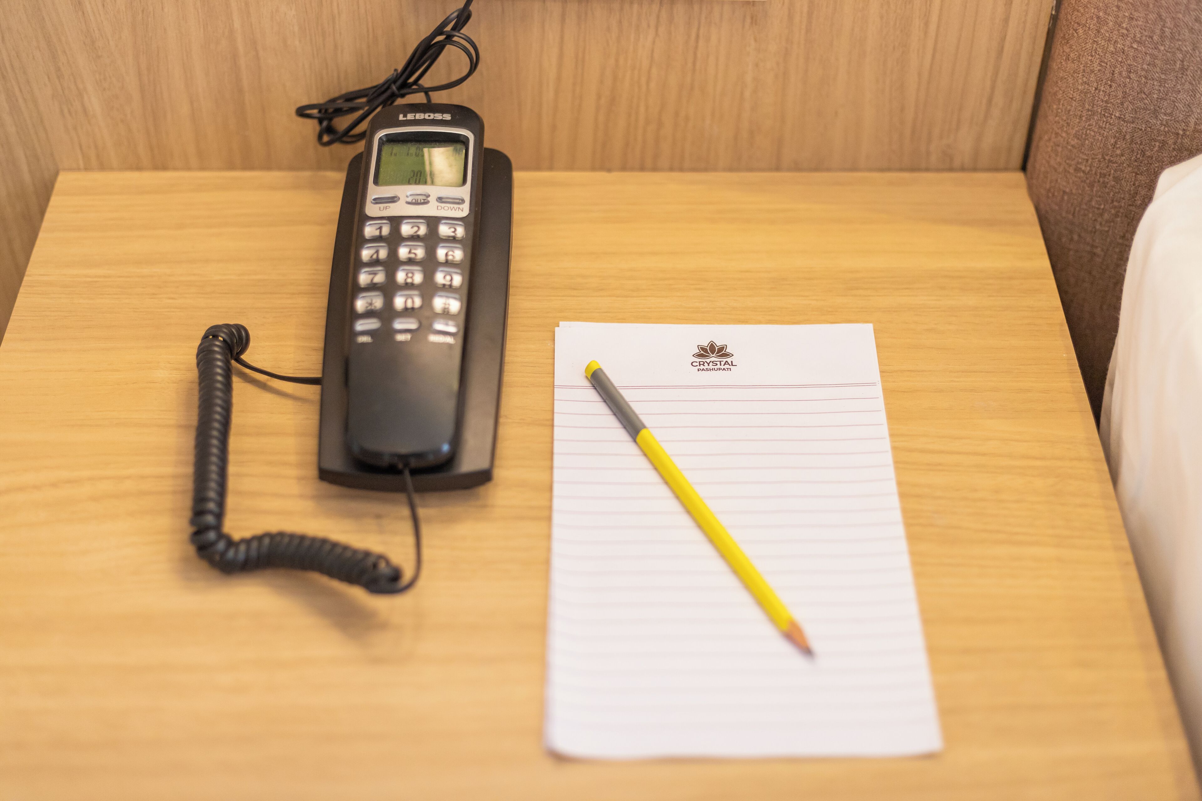 Una habitación de hotel con un teléfono, un bloc de notas y un lápiz sobre una mesa de madera.