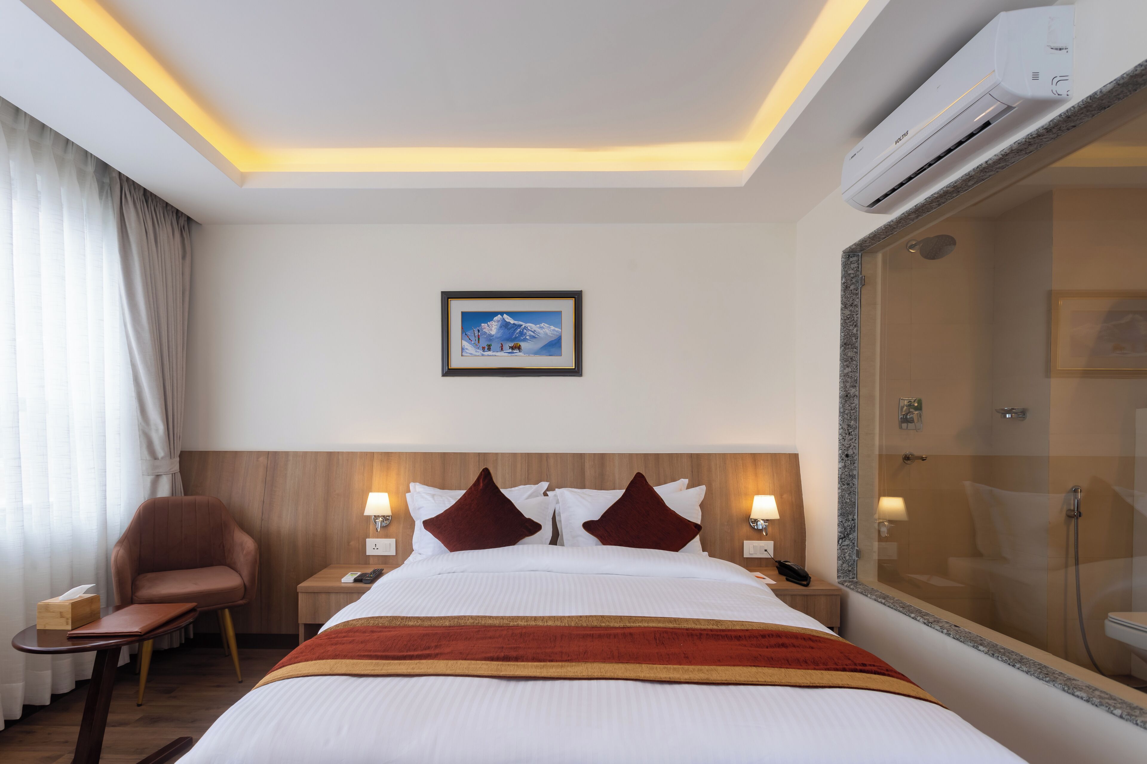 Una habitación de hotel con una cama, una silla, una mesita de noche con lámpara, un cuadro en la pared y un área de ducha.