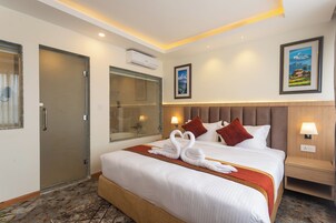 Una habitación de hotel con una cama grande, ducha, aire acondicionado instalado en la pared y un cuadro enmarcado.
