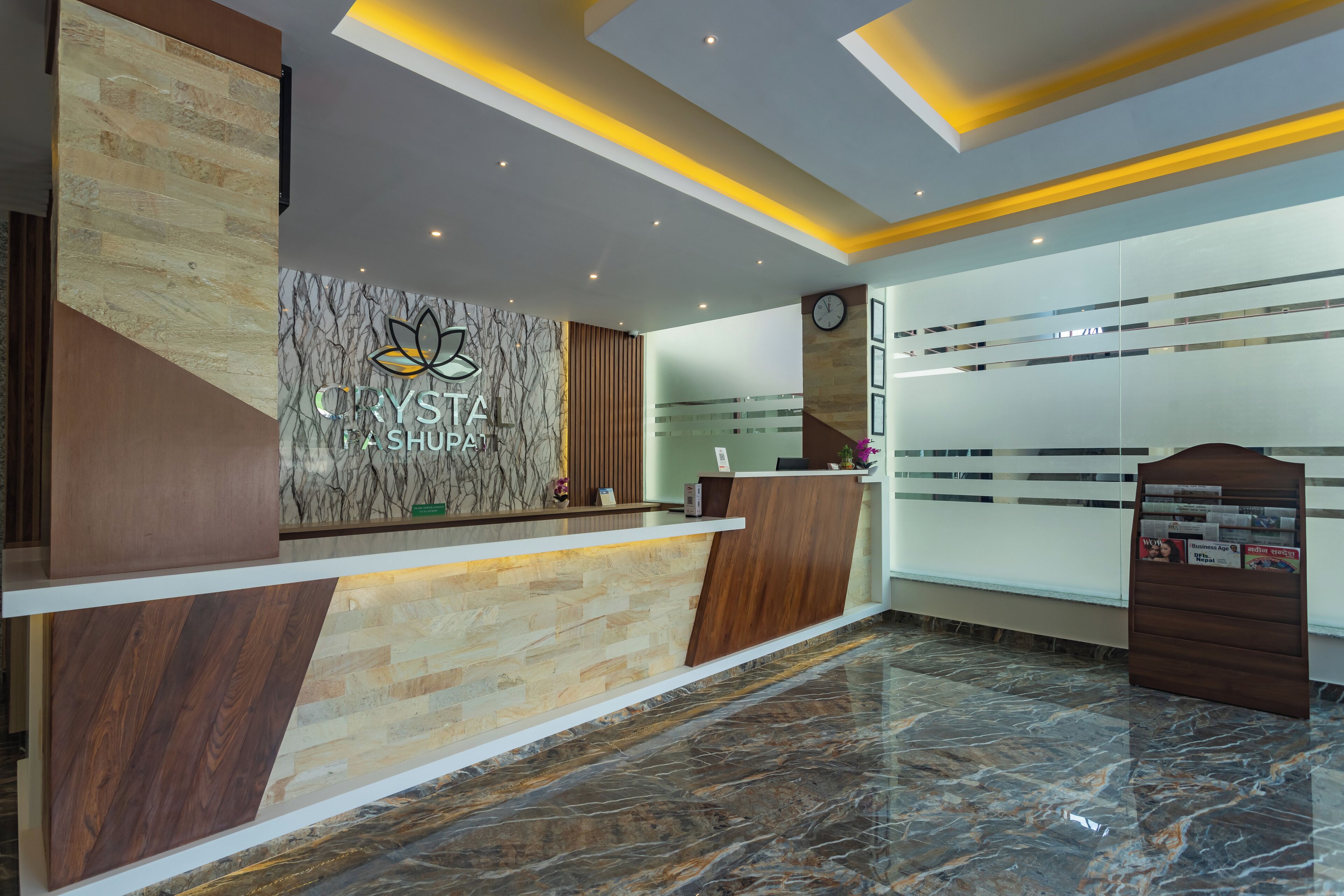 A reception desk with a logo, a clock, and a bulletin board in a modern hotel lobby.