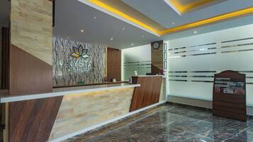 A reception desk with a logo, a clock, and a bulletin board in a modern hotel lobby.