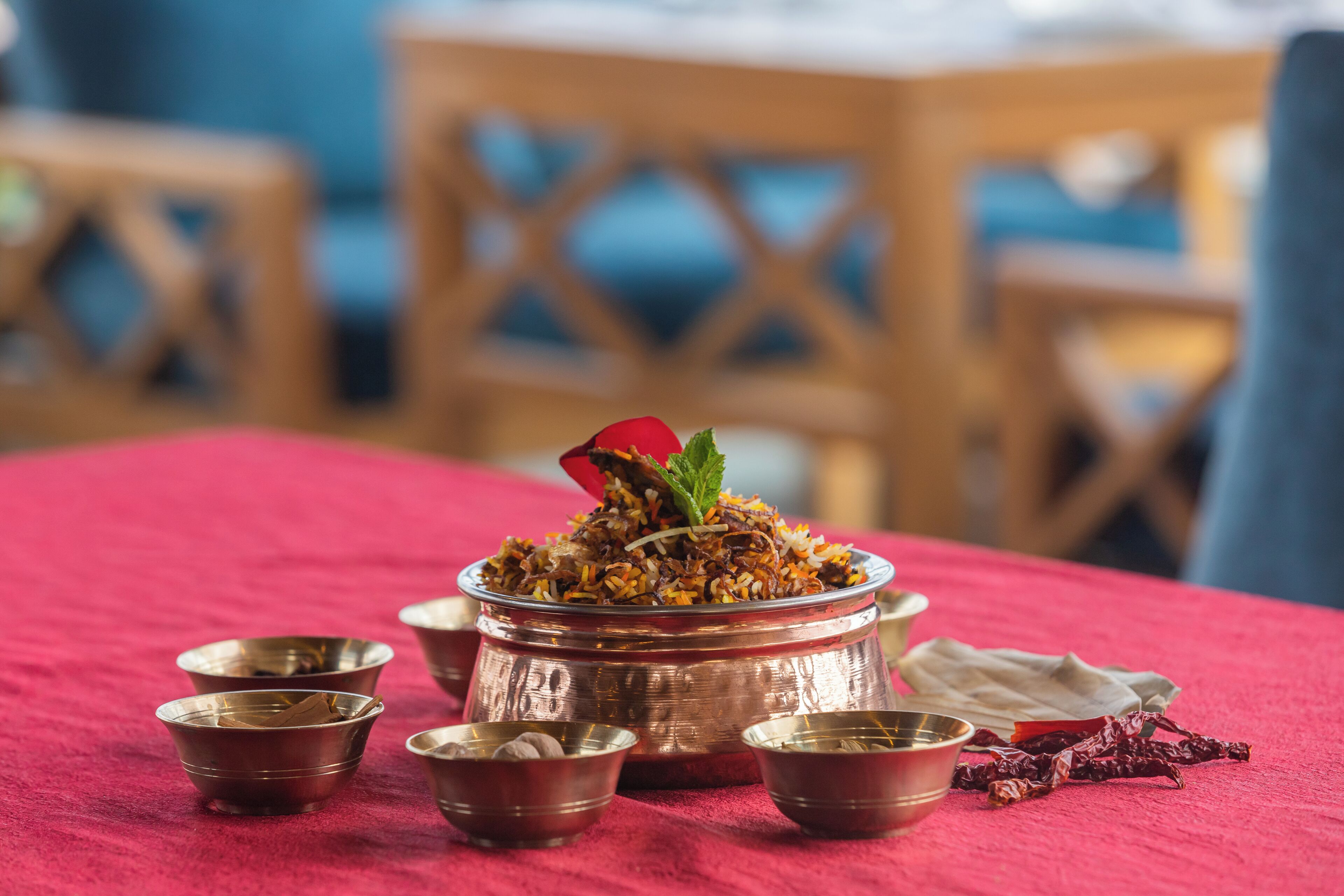 Un repas traditionnel, présenté dans un grand plat en cuivre rempli de biryani, accompagné de petits bols en métal et d’un tissu rouge.