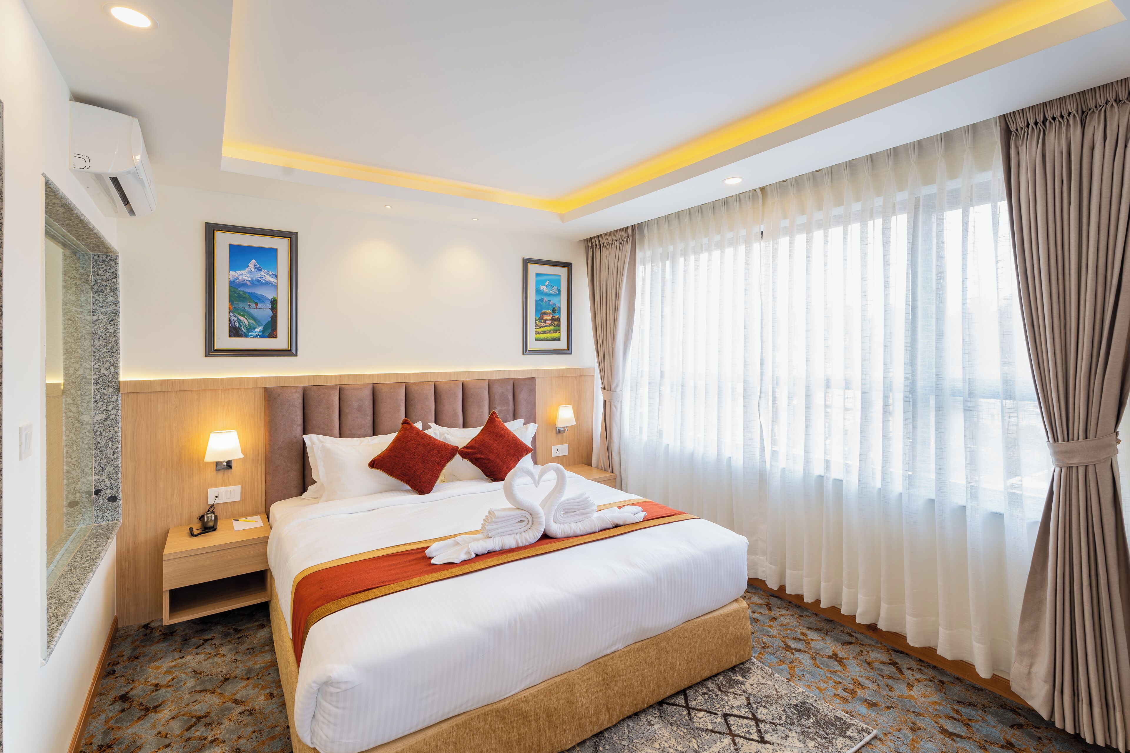 Une chambre d’hôtel avec un grand lit, deux oreillers, une tête de lit, une table de chevet, une lampe, un tableau encadré au mur et une fenêtre avec des rideaux.