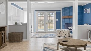 A spacious living area with a large window, a round coffee table, and a blue accent wall. - Updated Waterfront Pool Home with Putting Green (Cocoa Beach)