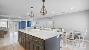 A spacious kitchen with a large island, white cabinetry, and pendant lighting. - Updated Waterfront Pool Home with Putting Green (Cocoa Beach)