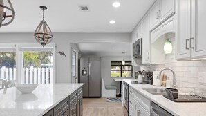A modern kitchen with a large island, stainless steel appliances, and a view to the outside. - Updated Waterfront Pool Home with Putting Green (Cocoa Beach)
