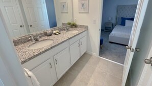 A bathroom with a granite countertop sink, white cabinets, and a large mirror.