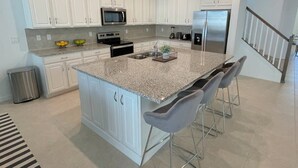 A modern kitchen with white cabinets, granite countertops, stainless steel appliances, and a central island with bar stools.