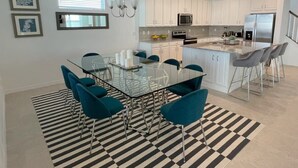 A modern kitchen with white cabinets, a glass dining table, teal chairs, and a black and white striped rug.