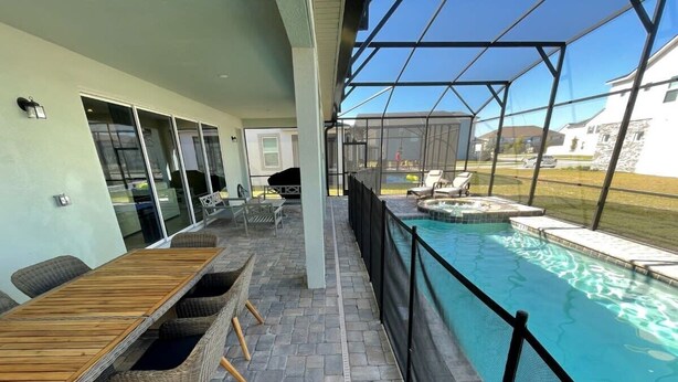 A covered outdoor area with a pool, wicker furniture, and a stone-tiled floor.