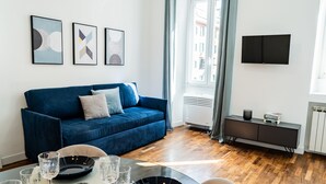 A modern living room with a blue sofa, a dining table with plates and glasses, and a flat-screen TV mounted on the wall. - Domina Apartments Roma - San Pietro 1 (Roma)
