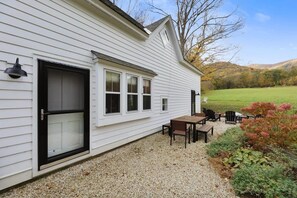 Une maison blanche avec une terrasse en gravier, une table en bois et deux chaises.