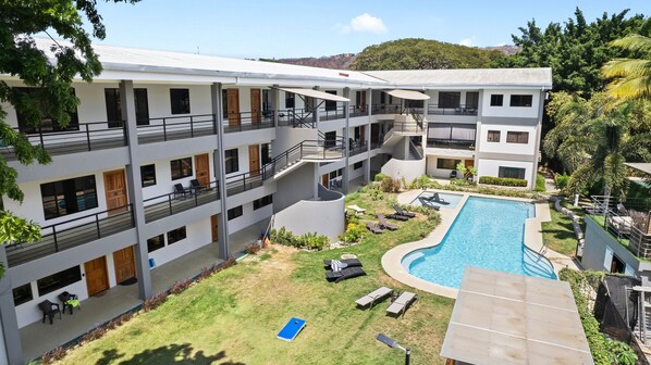 A multi-story hotel with a swimming pool, outdoor seating, and a lush garden. - Walk to Beach - Beach Gear & Games - Community Pool & Grill - Gated Complex w/Secure Parking (Playas del Coco)