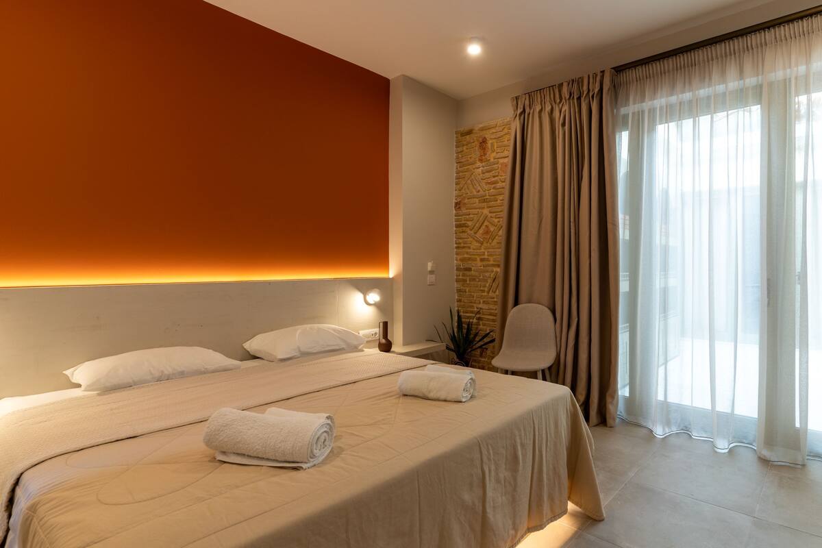 Una habitación de hotel moderna con una cama grande, una silla, un muro de acento de piedra y un amplio ventanal con cortinas.