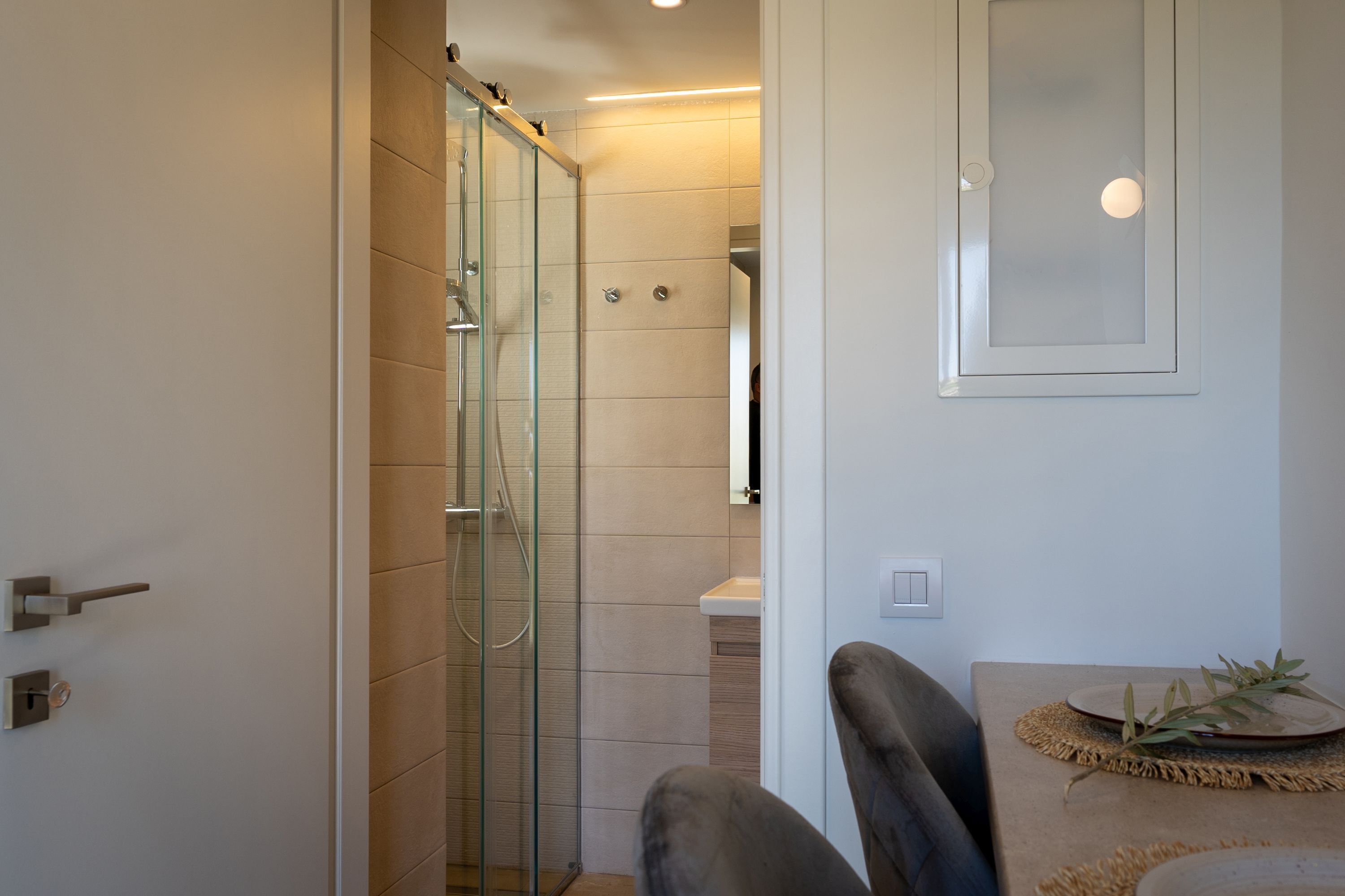 A bathroom with a glass shower enclosure, a sink, and a mirror.
