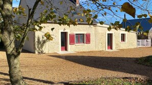 Un piccolo edificio in pietra con persiane rosse, un vialetto sterrato e un albero in primo piano.