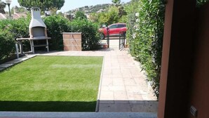 Um quintal com churrasqueira, um pátio pavimentado e um carro vermelho estacionado ao fundo.