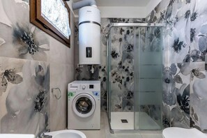 A bathroom with a washing machine, a shower with a glass door, and floral wall tiles. - A wonderful two-bedroom apartment situated just a short walk away from the sea in Costa Rei. (Costa Rei)