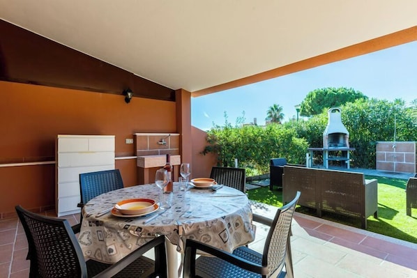 An outdoor patio with a round table, chairs, a grill, and a refrigerator. - A wonderful two-bedroom apartment situated just a short walk away from the sea in Costa Rei. (Costa Rei)