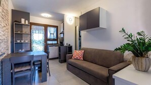 Um espaço compacto com cozinha compacta, sofá, mesa de jantar com cadeiras e um vaso com planta.