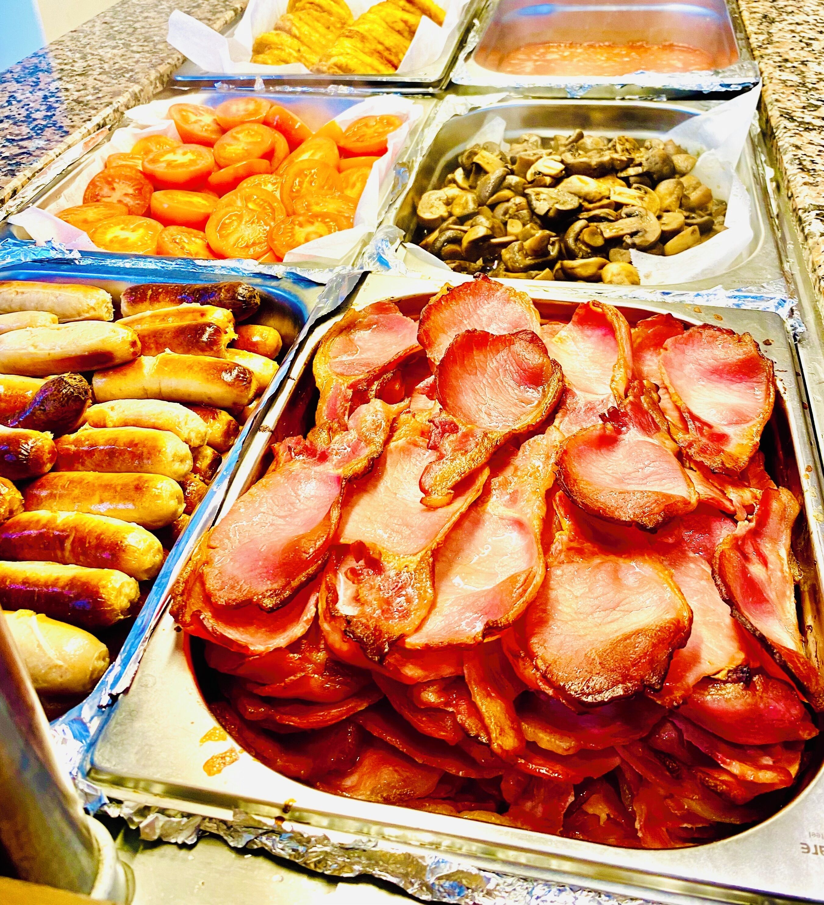 A buffet with various food items including ham, sausages, tomatoes, and mushrooms.