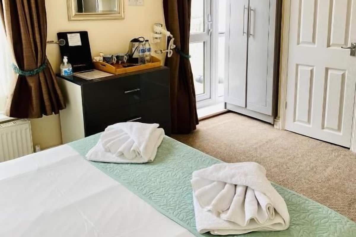 A hotel room with a bed, a bedside table with a lamp, a mirror, a wardrobe, and a door to a balcony.