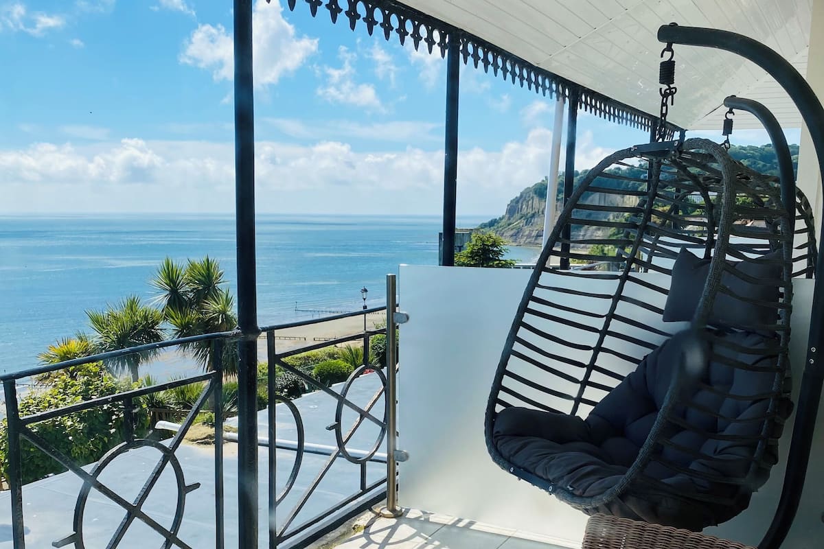A balcony with a hanging chair, a wicker sofa, and a view of the sea.