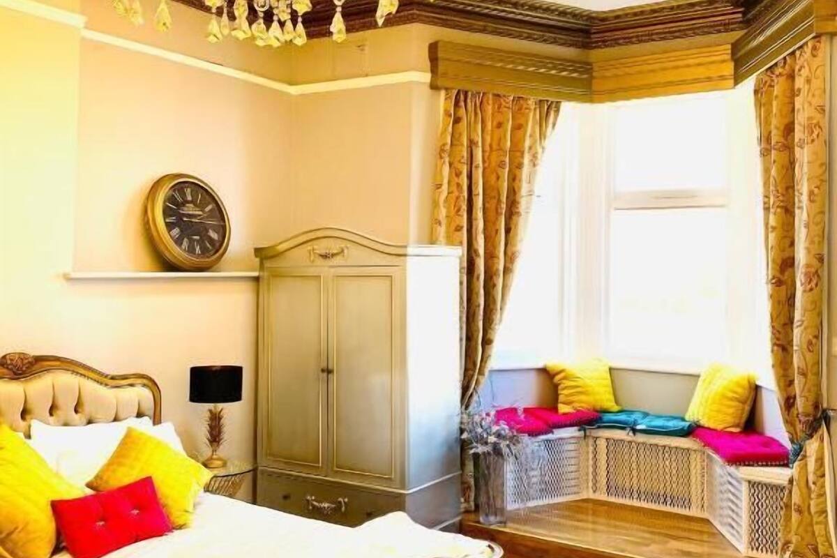 A bedroom with a bed, a nightstand, a wardrobe, a window with curtains, and a chandelier.