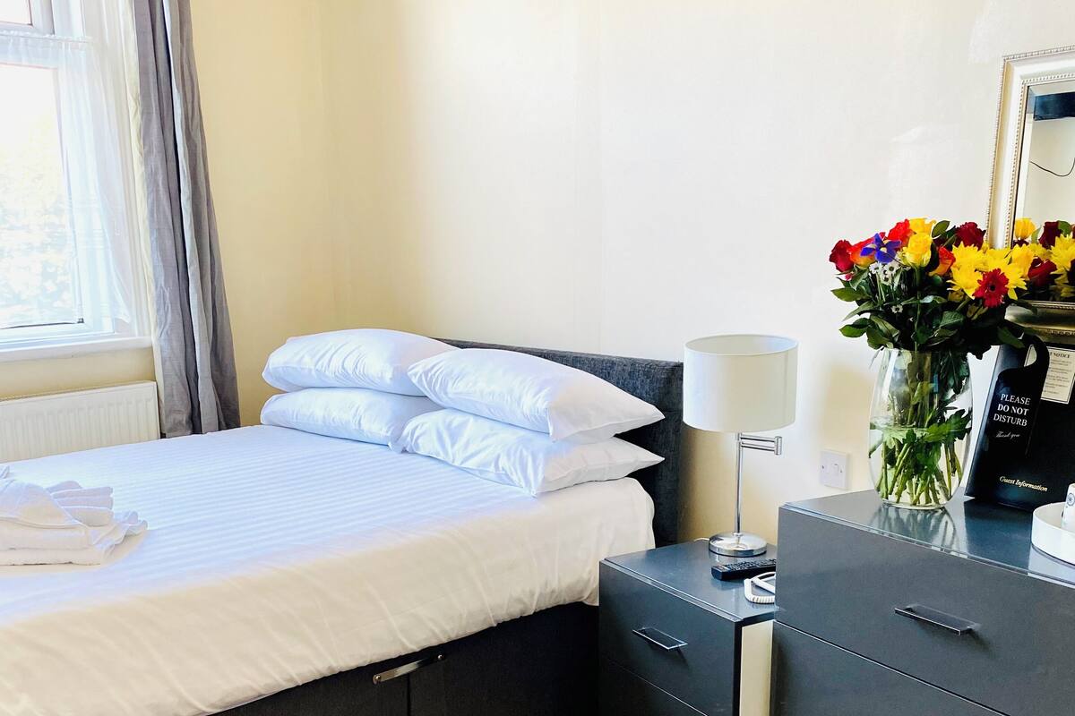 A neatly made bed with white linens, a bedside table with a lamp, and a vase of flowers.
