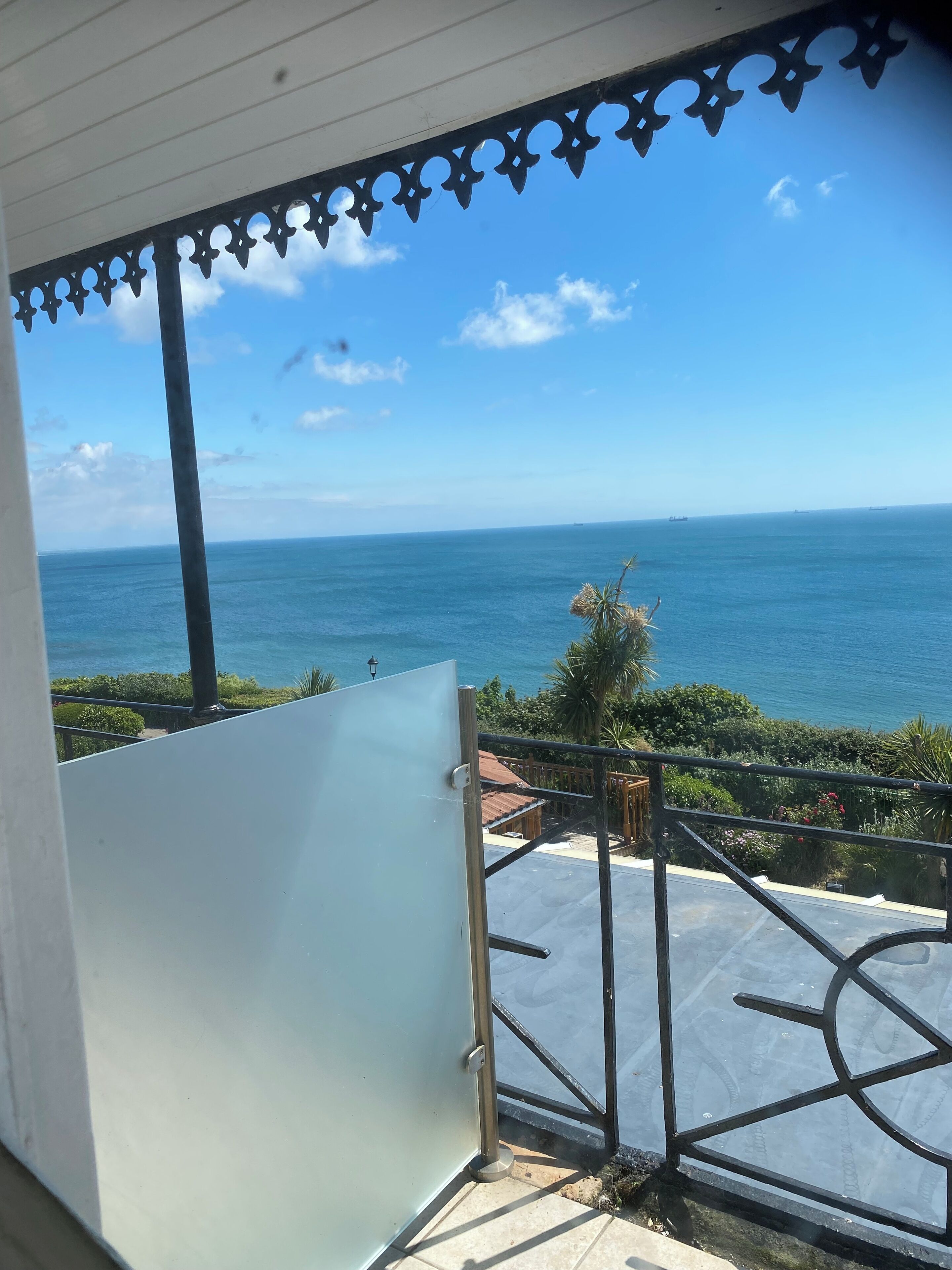 A balcony with a view of the ocean, a metal gate, and a tiled floor.