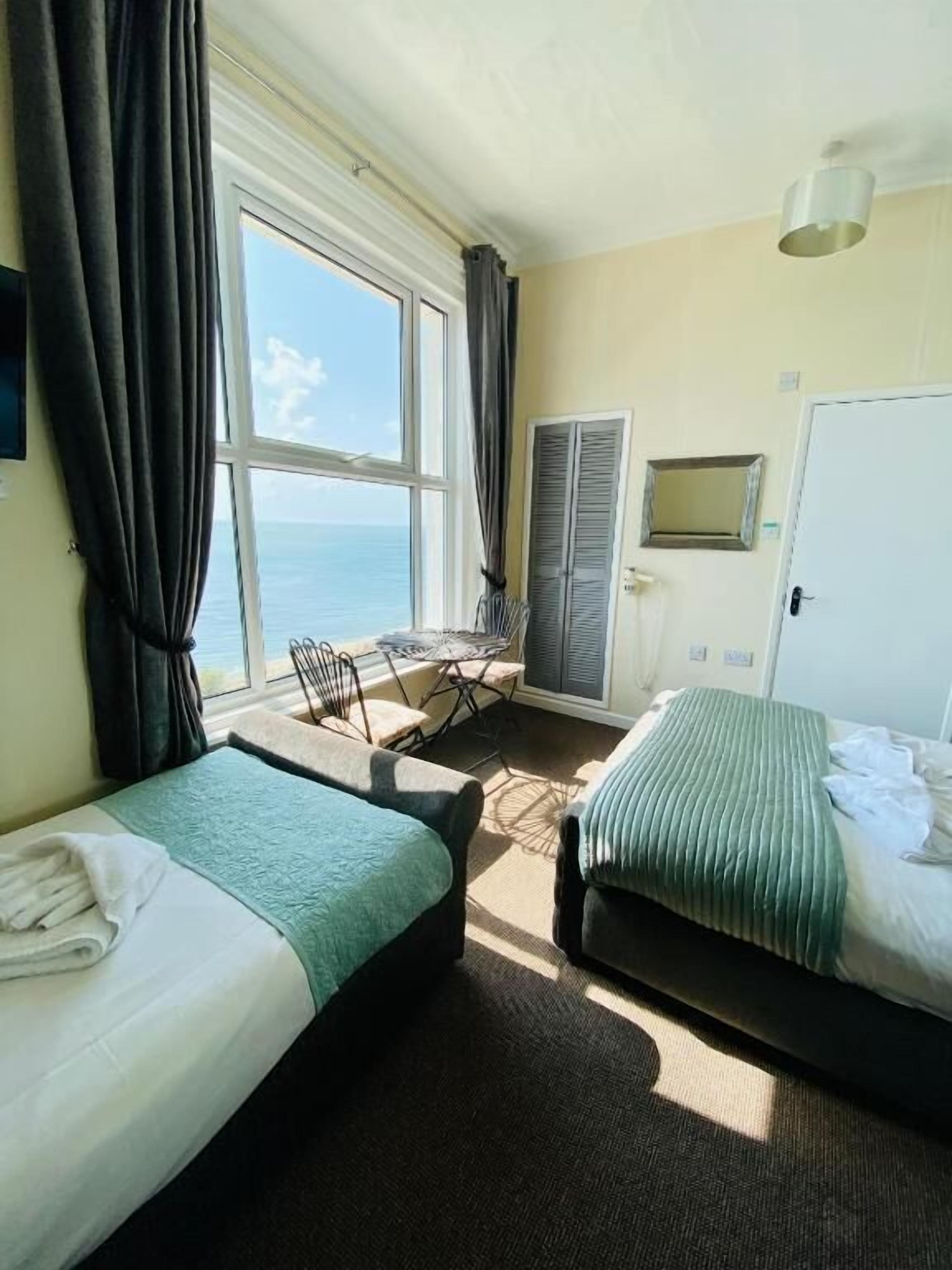 Una habitación de hotel con dos camas, un escritorio y vista al mar.