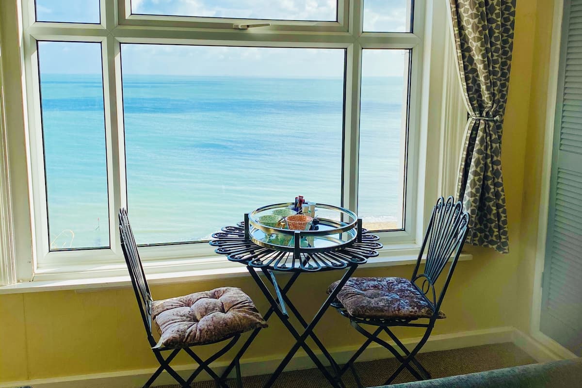 A room with a large window offering a view of the ocean. There is a round table with chairs and a small decorative item on it.