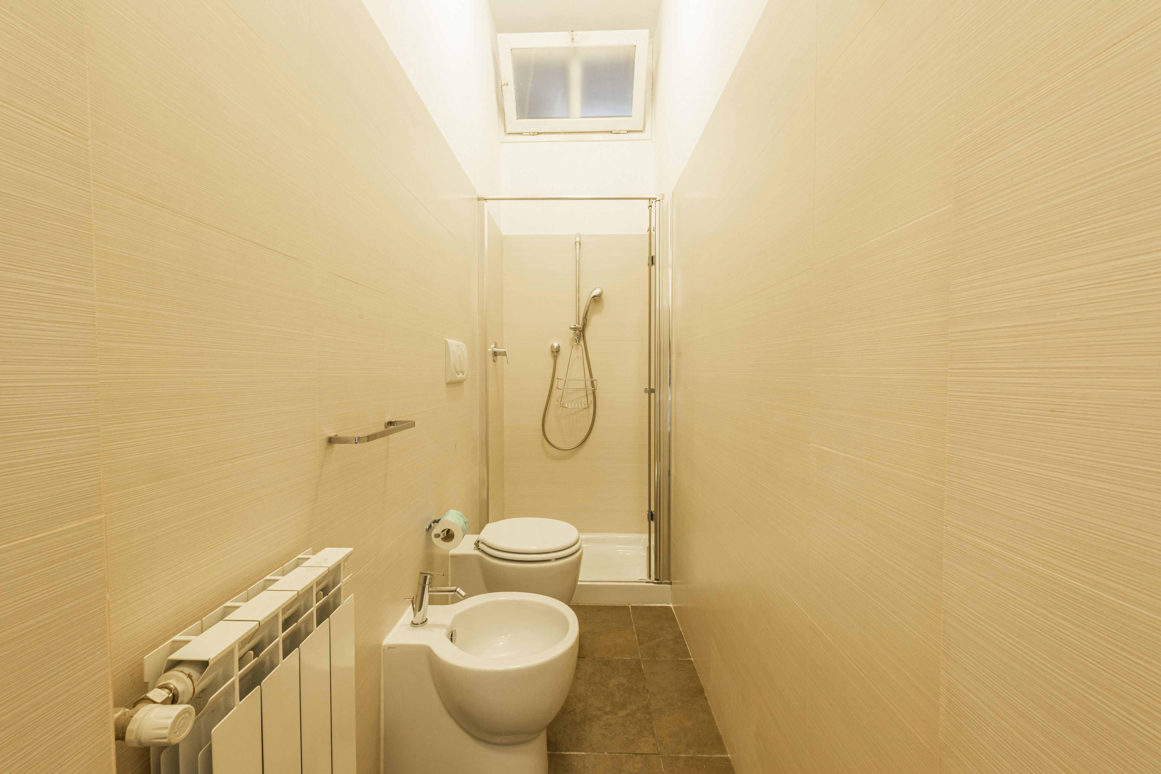 Een smalle badkamer met toilet, bidet en douche.