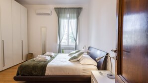 A bedroom with a bed, a bedside table, a lamp, a window with curtains, and a wardrobe. - Casa Zamia by Mmega (Florence)