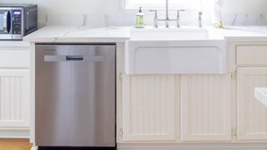 A kitchen with white cabinetry, a stainless steel dishwasher, a microwave, and a sink with a window above it. - Bridal Ready + Southern Charm | The Moli (La Grange)