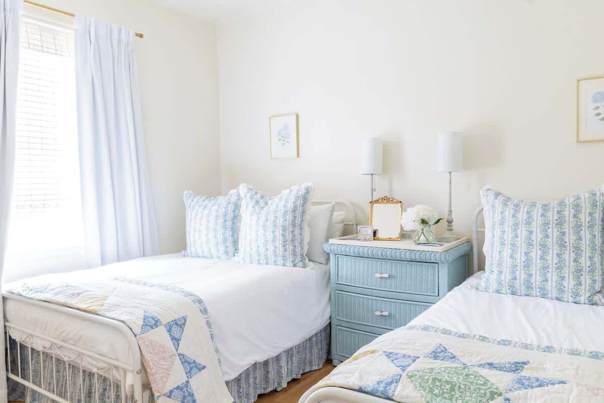 Un dormitorio con dos camas, una mesita de noche y un ventanal con cortinas.