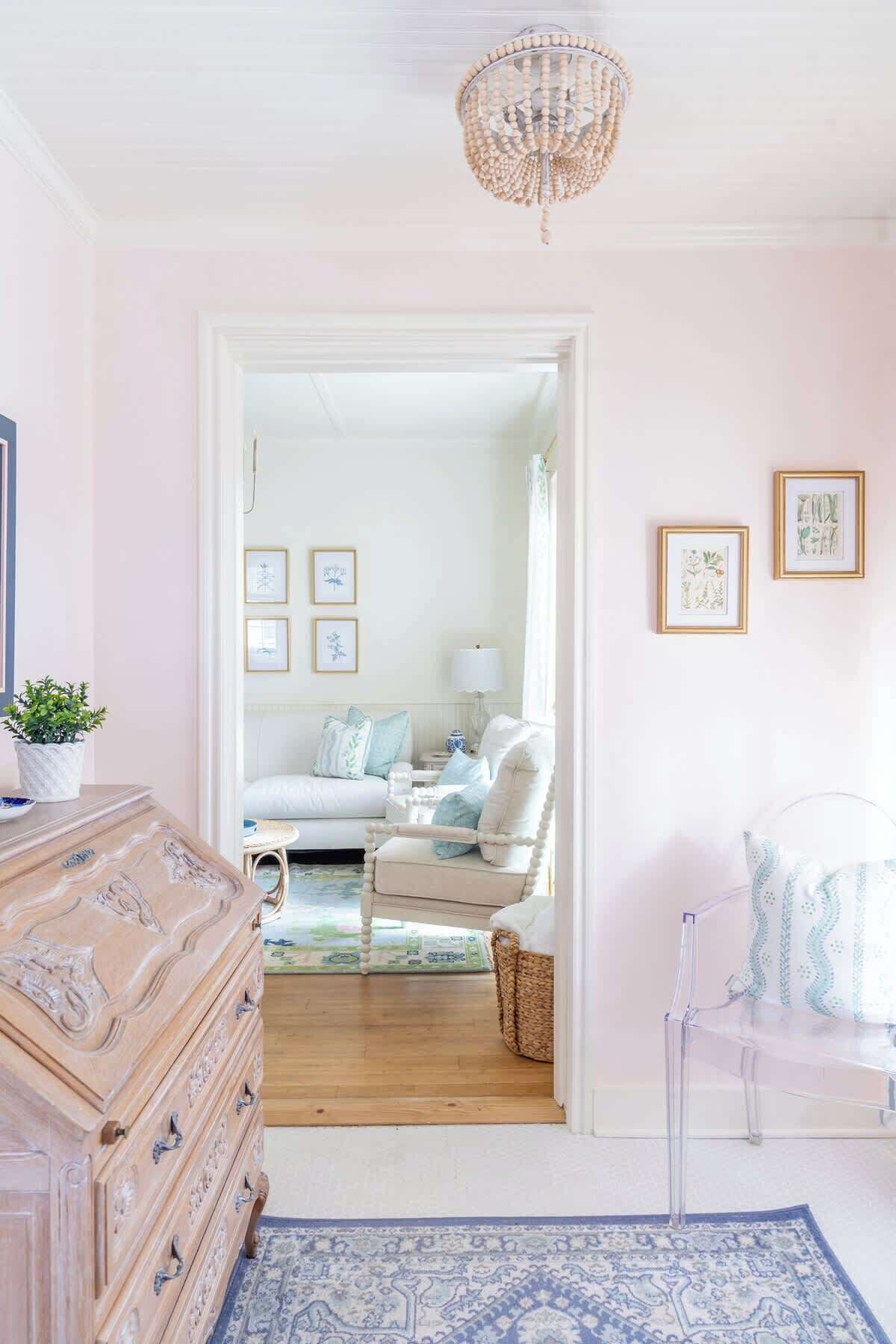 A room with a wooden dresser, a clear chair, a white sofa, and a patterned rug.
