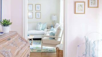 A room with a wooden dresser, a clear chair, a white sofa, and a patterned rug.