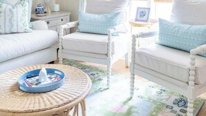 A bright, airy room with a white sofa, two white armchairs, a wicker coffee table, and a patterned rug. - Bridal Ready + Southern Charm | The Moli (La Grange)