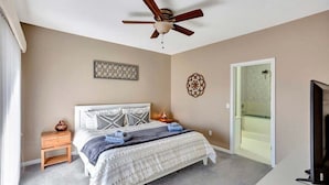 A bedroom with a bed, a ceiling fan, a nightstand, a TV, and a door leading to a bathroom.