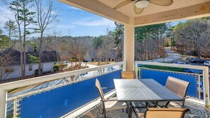 A covered balcony with a table and chairs, overlooking a residential area with houses and trees.