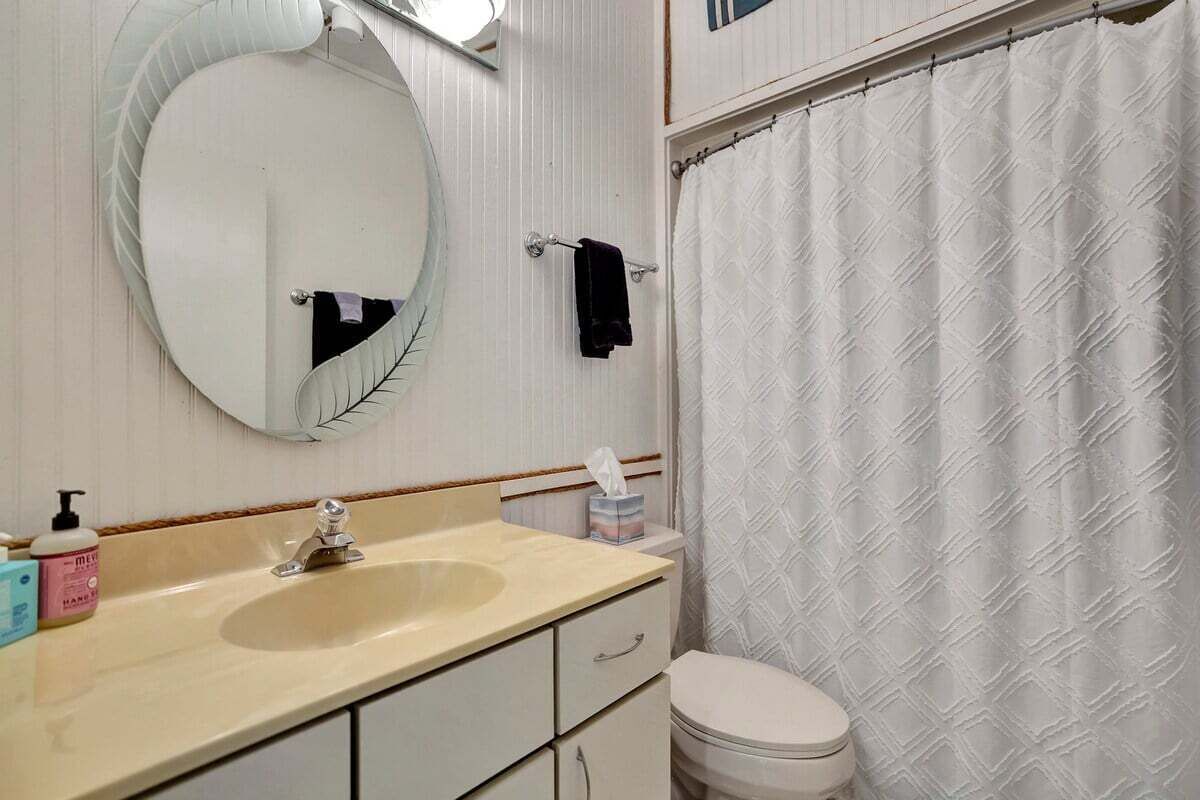 A bathroom with a round mirror, a sink, a toilet, and a shower curtain.