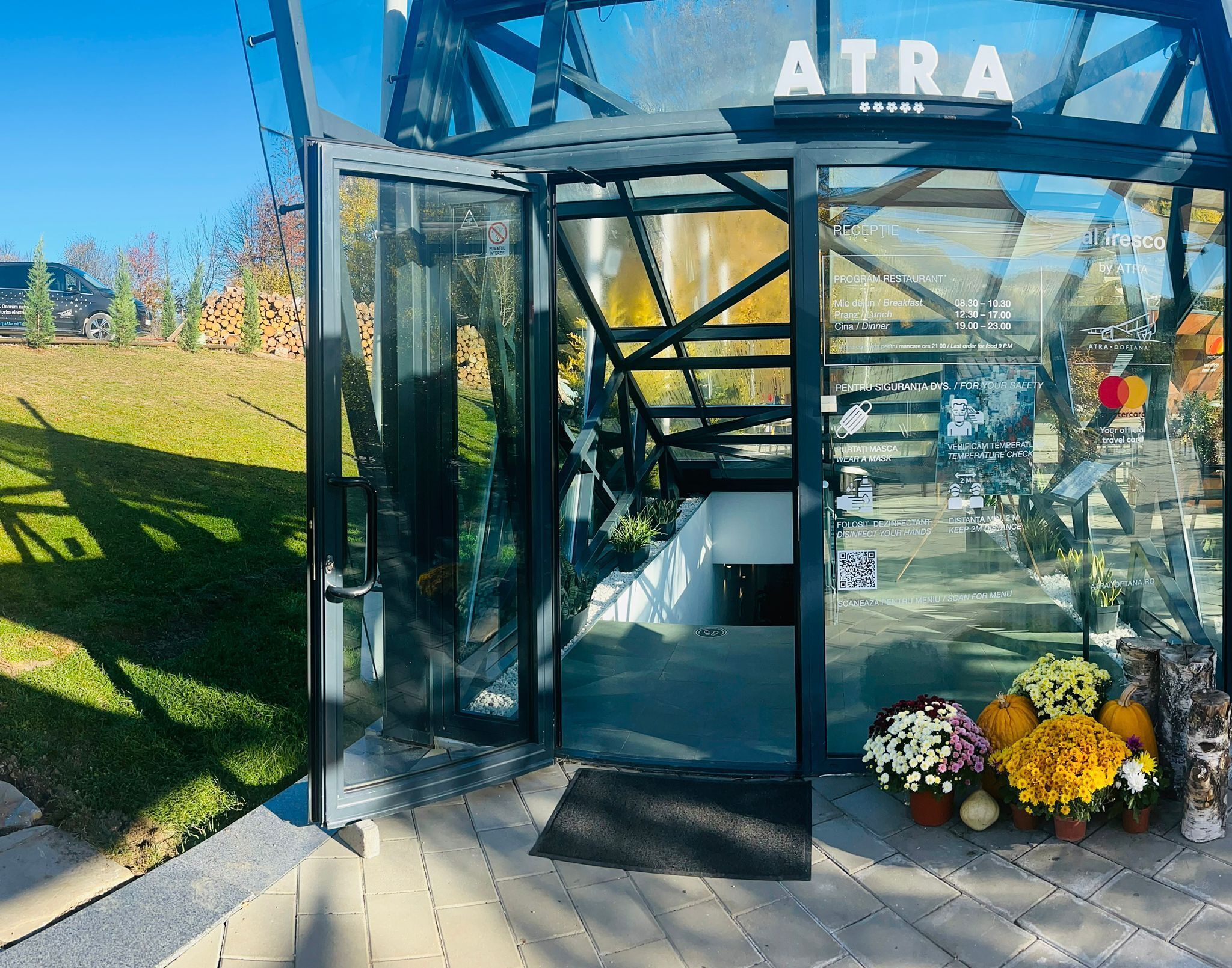 A glass entrance to a restaurant with a clear view of the outdoor area, including a stack of firewood and a grassy lawn.