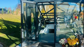 A glass entrance to a restaurant with a clear view of the outdoor area, including a stack of firewood and a grassy lawn.