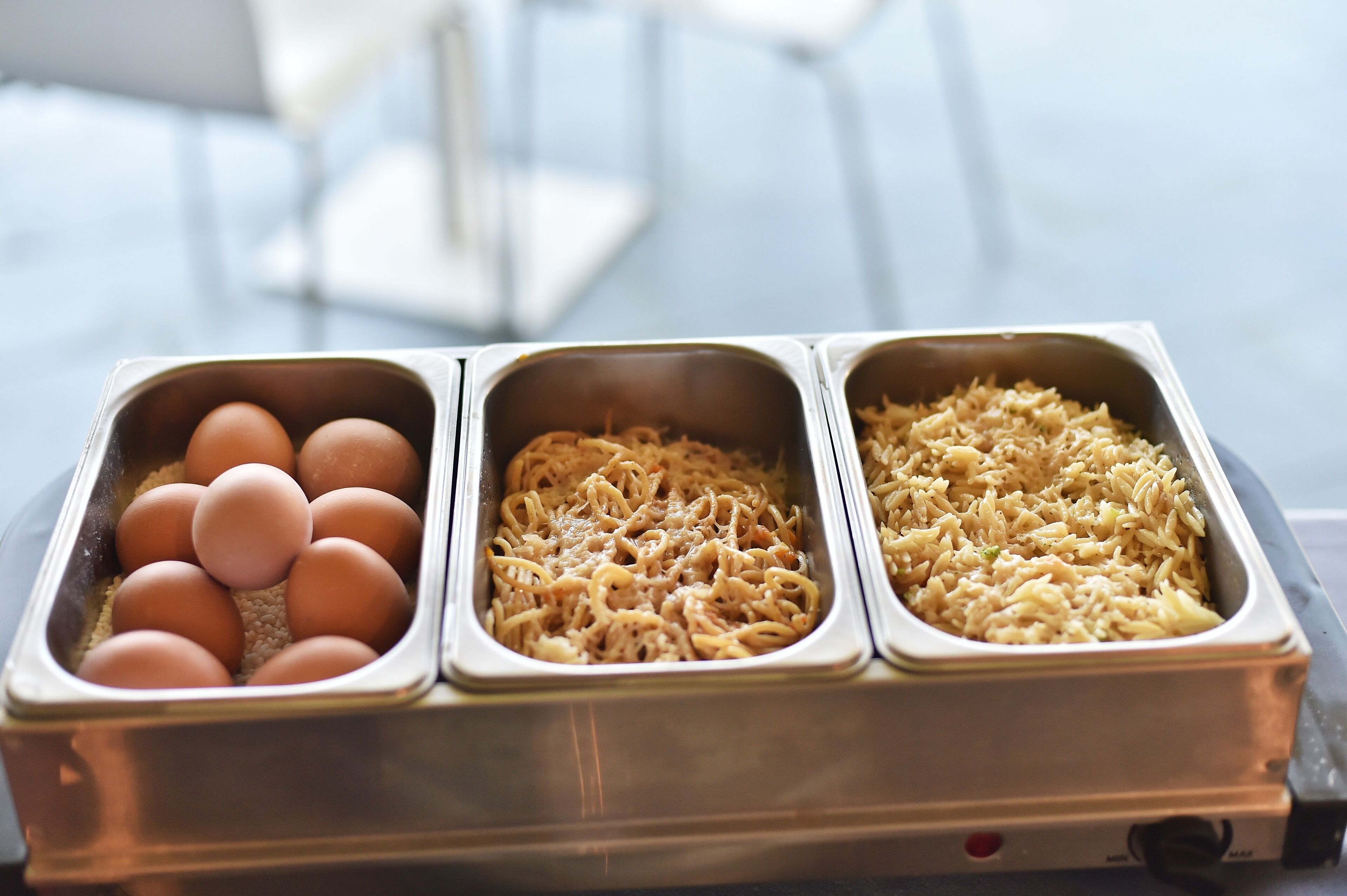 Un bufé con tres fuentes que ofrecen huevos, fideos y pasta.